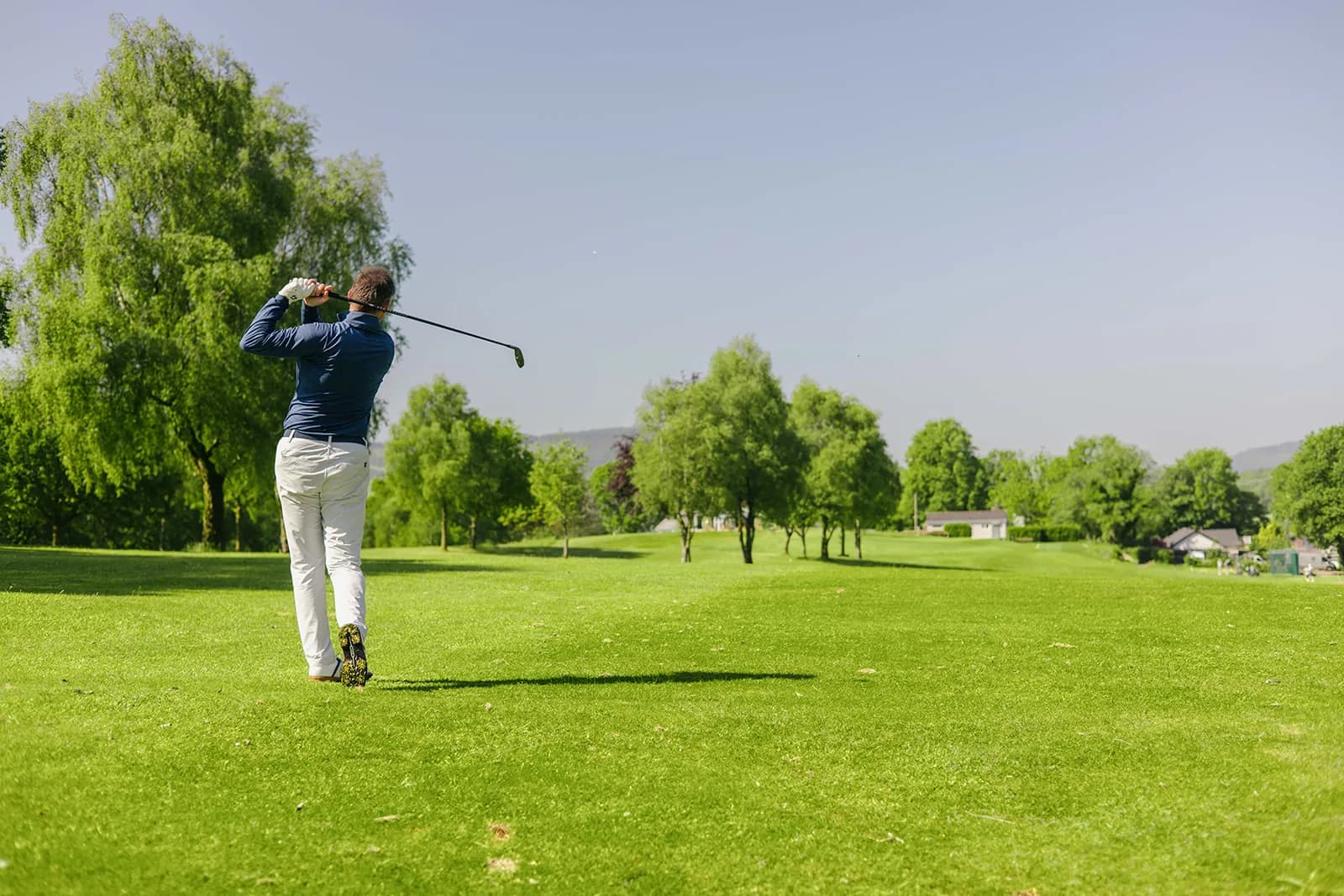 Stuart Wilson finishing an iron shot on an open parkland fairway lined with mature trees