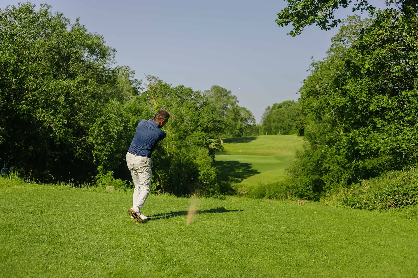 Stuart Wilson playing a tee shot down a narrow, tree lined hole